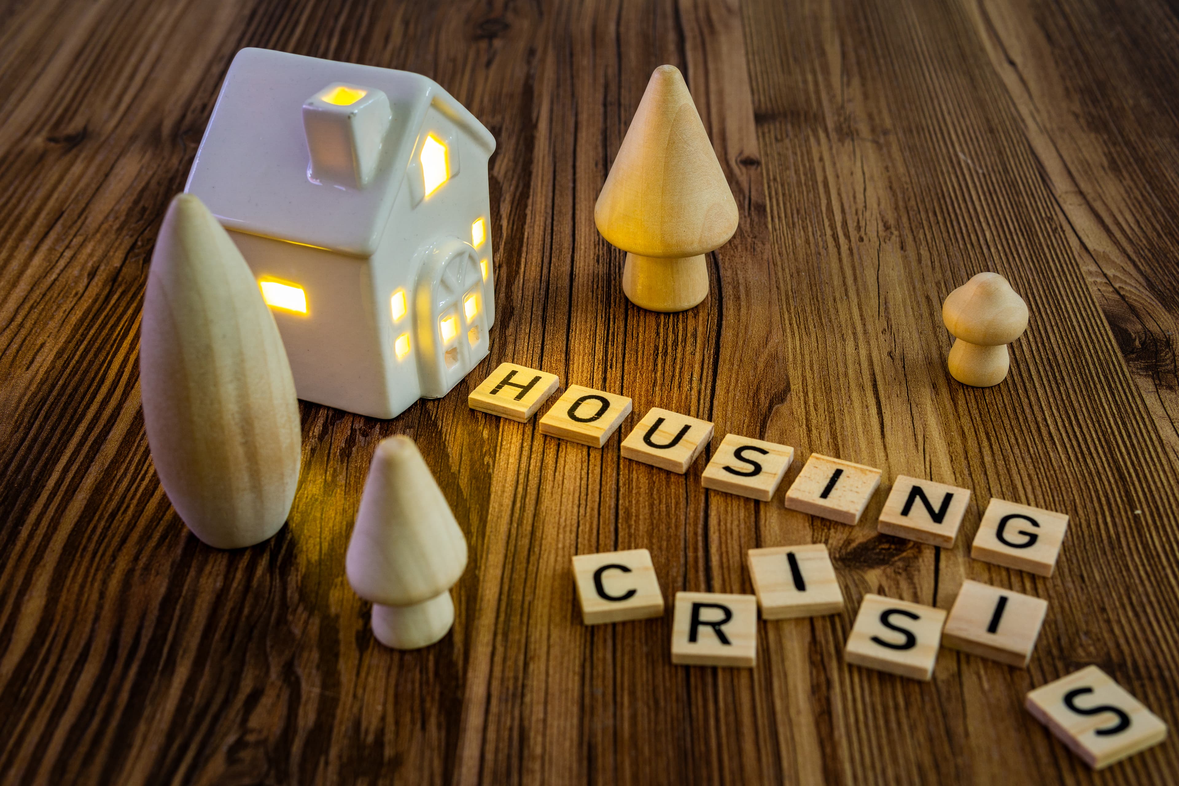 Wooden blocks spell housing crisis with a small house model.