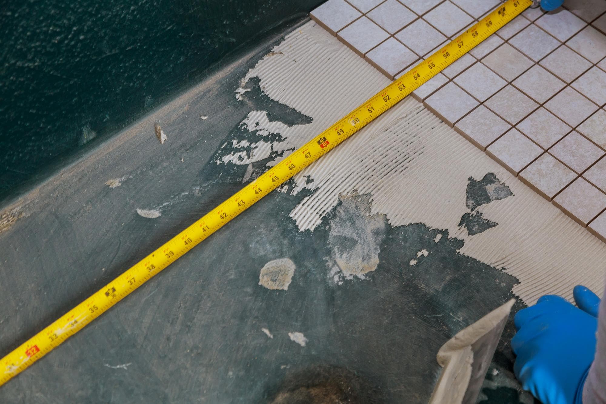 Bathroom floor showing waterproofing failure with missing tiles and exposed underlayment.